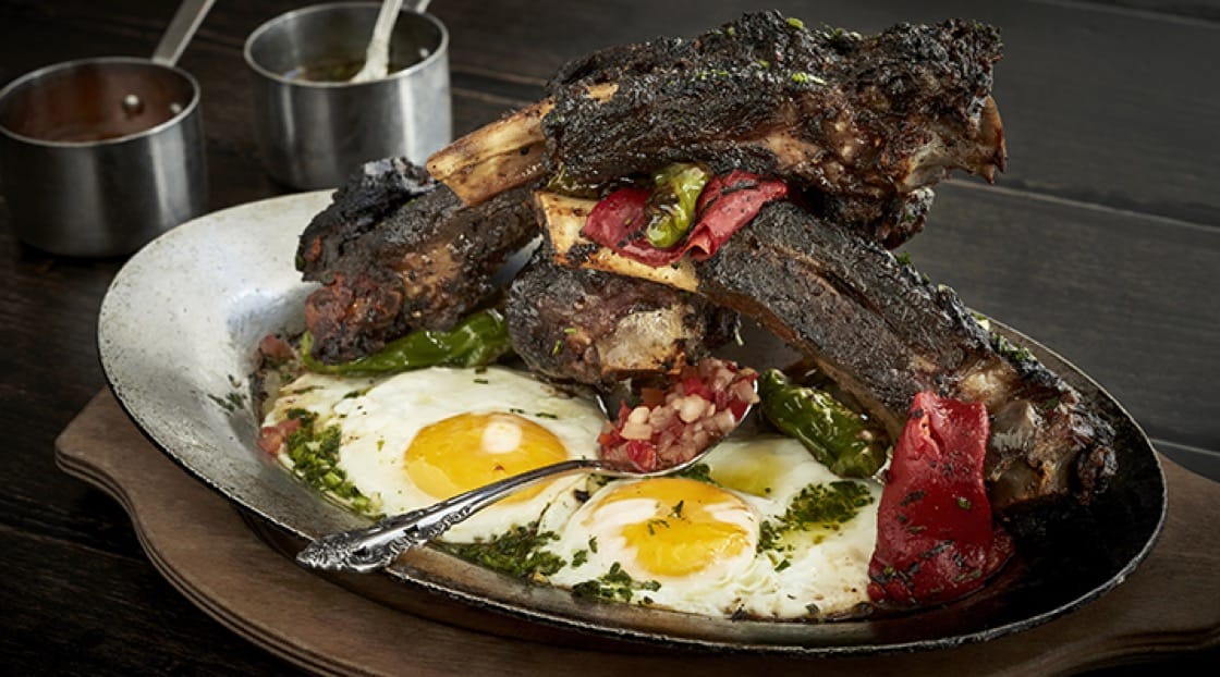 Roasted dry-aged beef ribs with aji amarillo spiced, grilled eggs and chimichurri. Photo by Greg Powers.