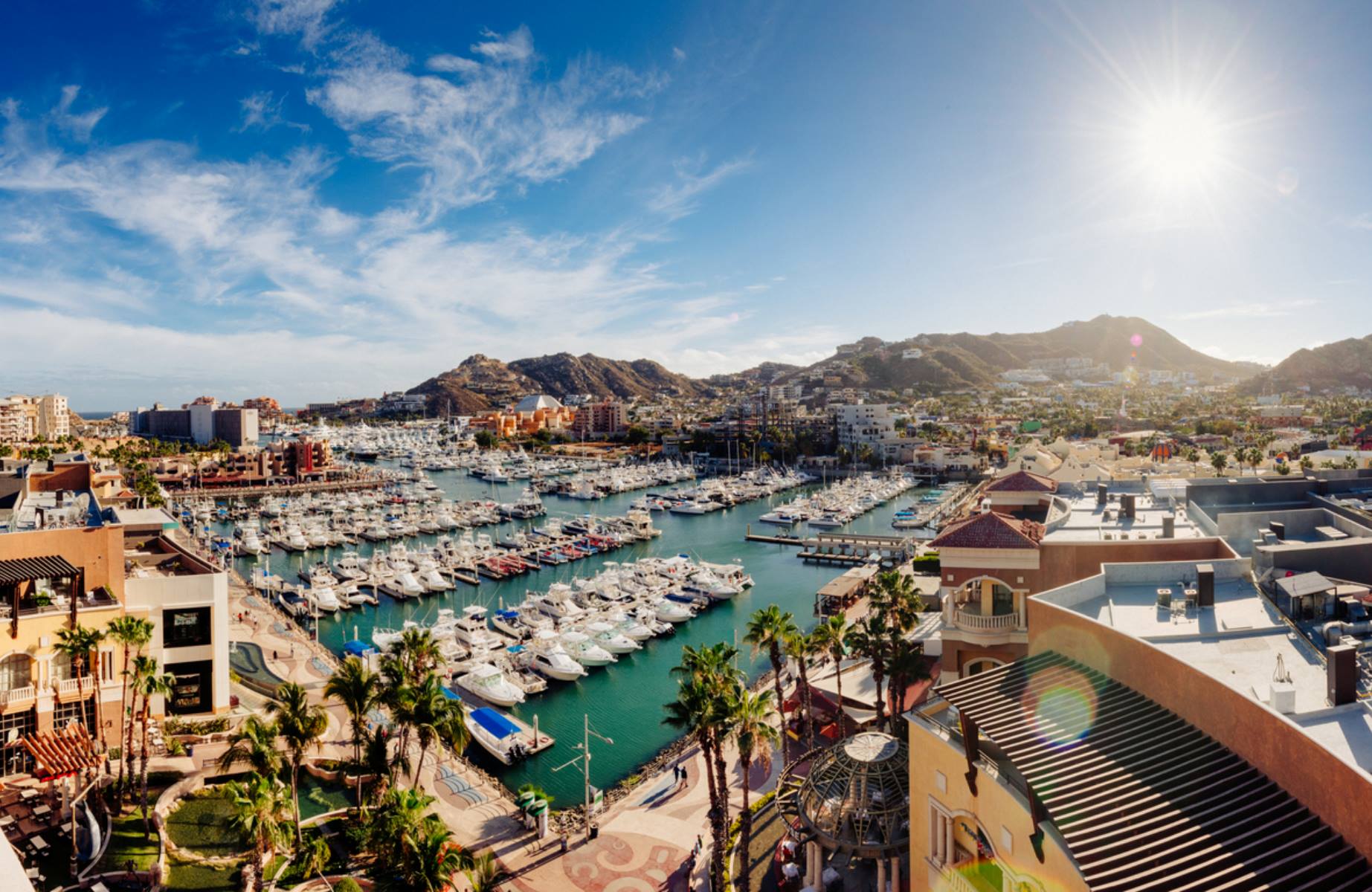 A sun-drenched marina filled with boats sparkles against the backdrop of rugged hills and coastal buildings in Mexico’s scenic Baja Peninsula ©ferrantraite/iStock