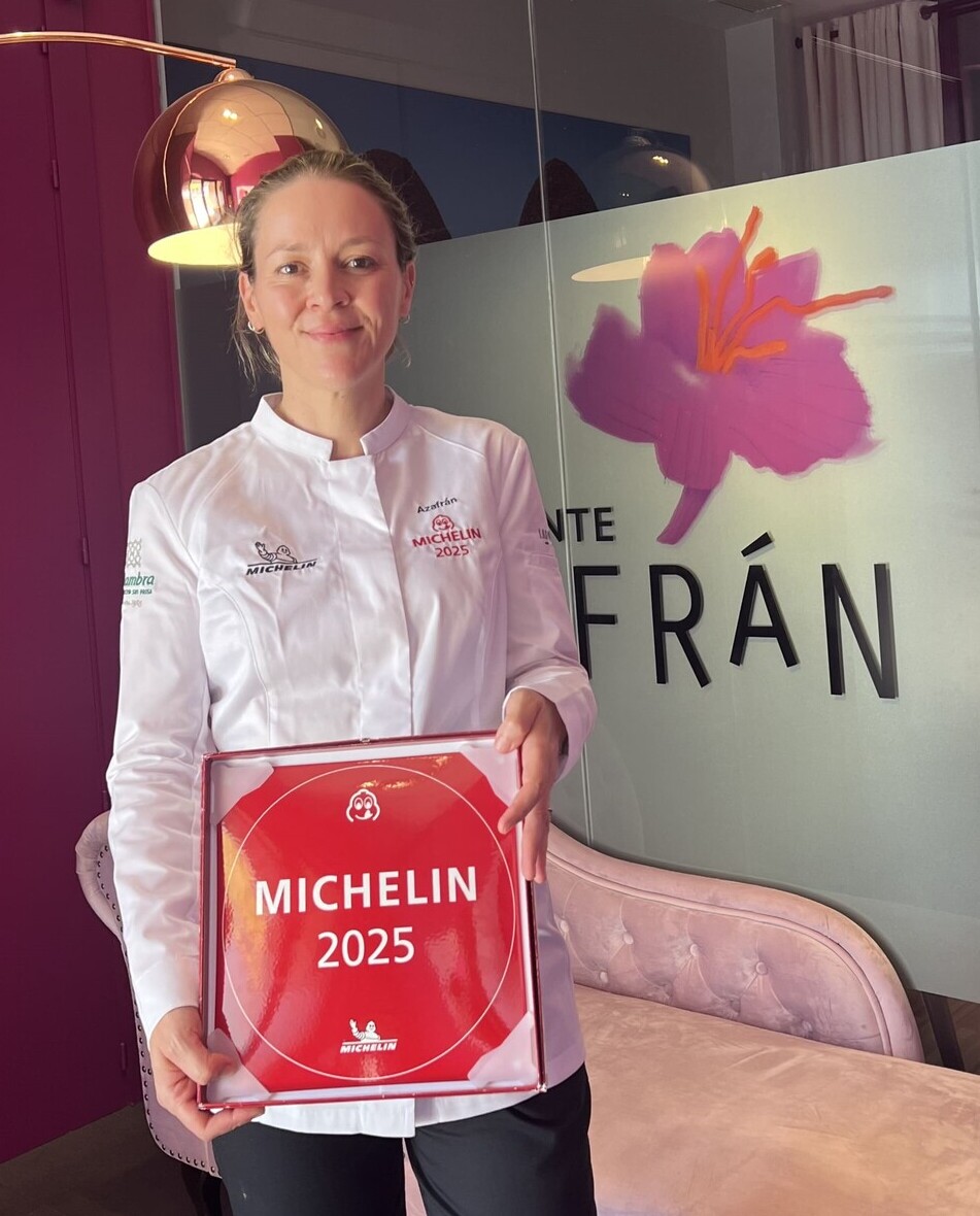 La chef Teresa Gutiérrez, a la entrada del restaurante, con la chaquetilla y la placa MICHELIN 2025. © Azafrán