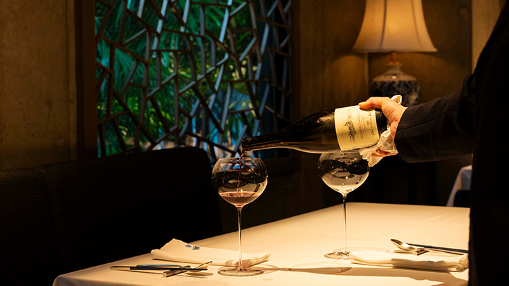 クラシックな中国の雰囲気が感じられるインテリアの店内。ワインを注ぐ熊谷さん　© Hisashi Yoshino / The MICHELIN Guide