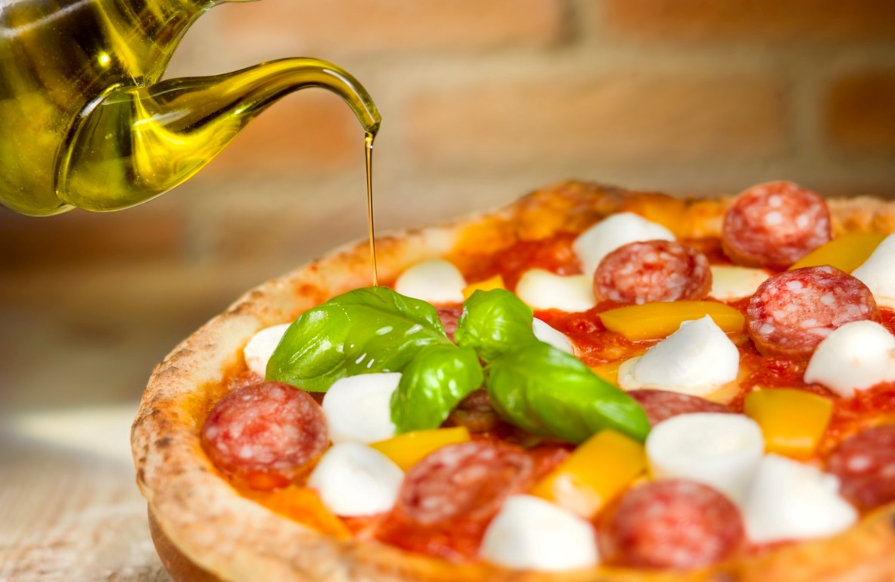 Pizza italiana con pomodori, mozzarella, peperoni, salame e basilico, con olio extravergine versato a filo, ©fcscaffeine/iStock