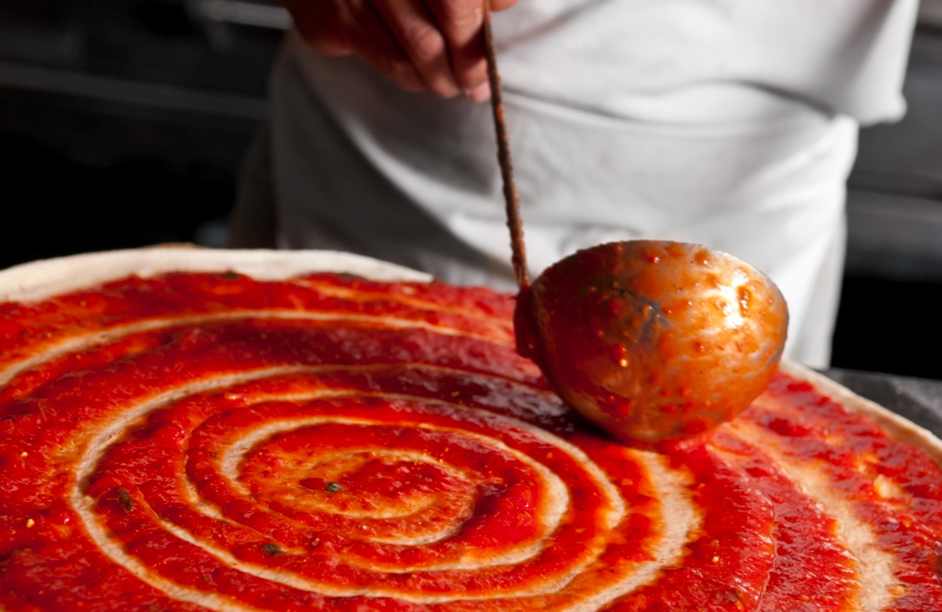 Salsa di pomodoro stesa sulla pizza con un mestolo. ©rudisill/iStock