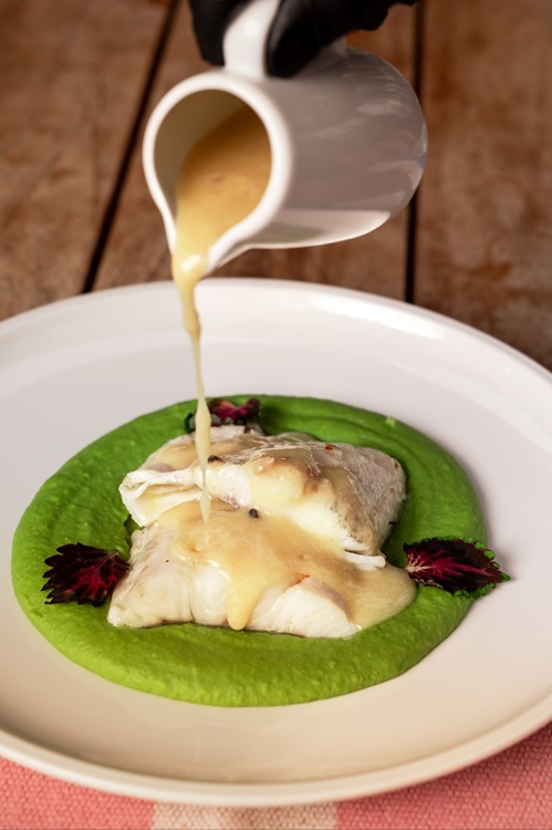 Silky sauce cascading over tender fish, resting on a vivid green embrace. © Suvenir 