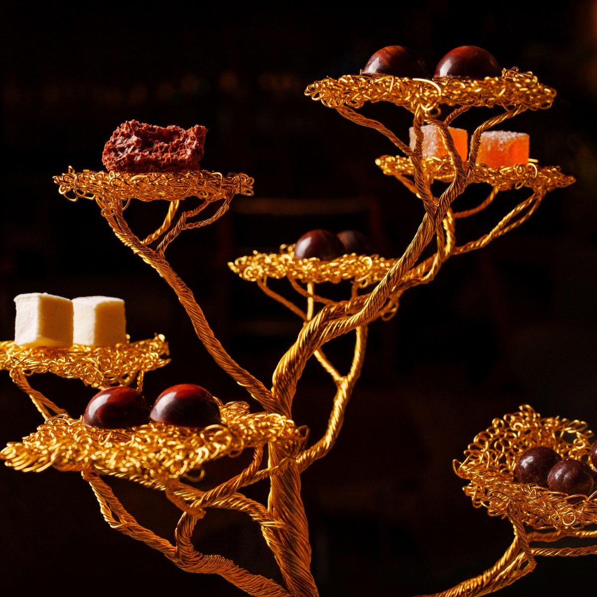Os galhos de uma árvore artesanal, feita com fios dourados, servem de cenário para que o restaurante Tuju, agora com três Estrelas MICHELIN, apresente alguns de seus doces de chocolate, elaborados na própria cozinha. © Rubens Kato/Tuju 