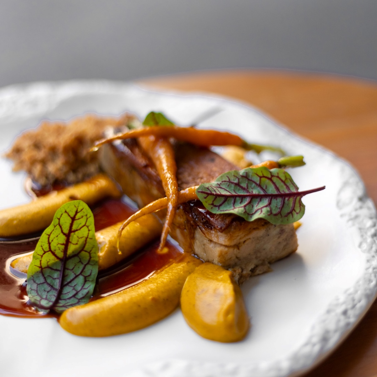 Suculento Leitãozinho cozido em baixa temperatura, emulsão de cenouras queimadas na brasa, baby cenouras glaciadas e farofa de alho do restaurante Tanit, novo Bib Gourmand de São Paulo. © Juliana Primon/Tanit