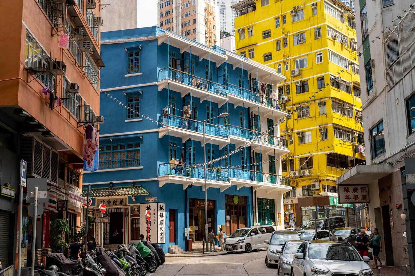 Blue House Cluster in Wan Chai framed by colorful high-rises, narrow streets, and everyday city life at ground level. © Shutterstock