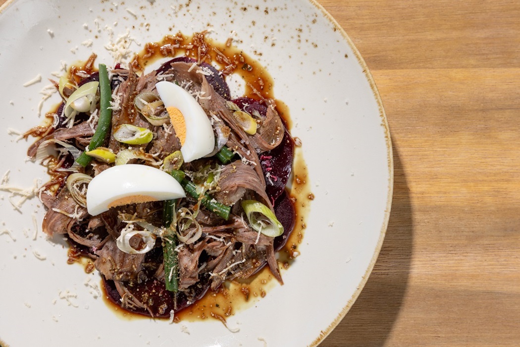 A beautifully plated dish featuring tender shredded meat, beetroot, soft‑boiled eggs, and fresh spring onions, finished with a rich. © DEAN DUBOKOVIC Gostilna Francl