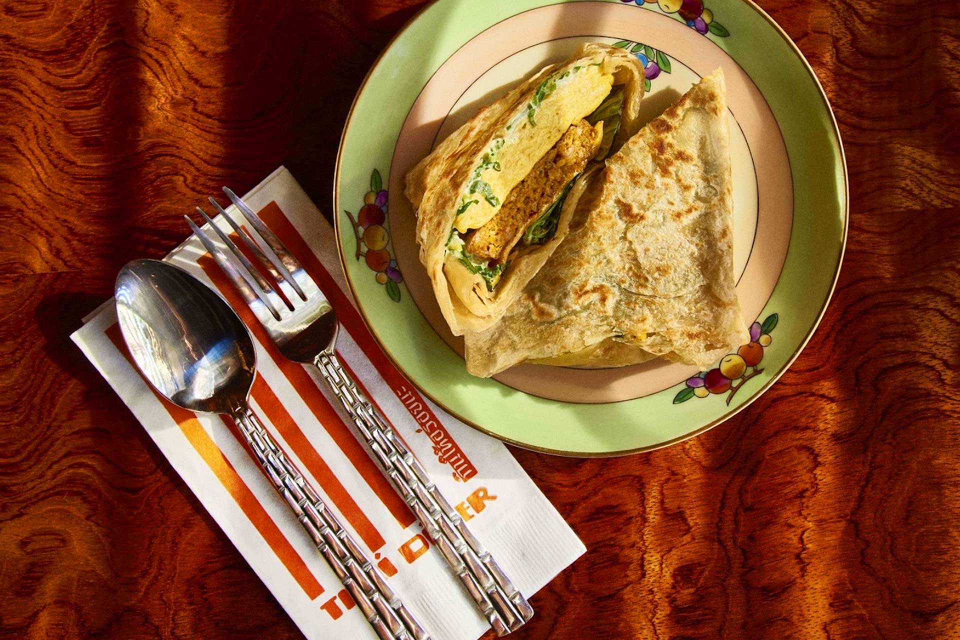 Thai Diner's egg sandwich is a tidy roti-wrapped creation filled with egg crepe, American cheese, herbal sai oua sausage, a smear of scallion mayo and fresh Thai basil leaves. © Thai Diner