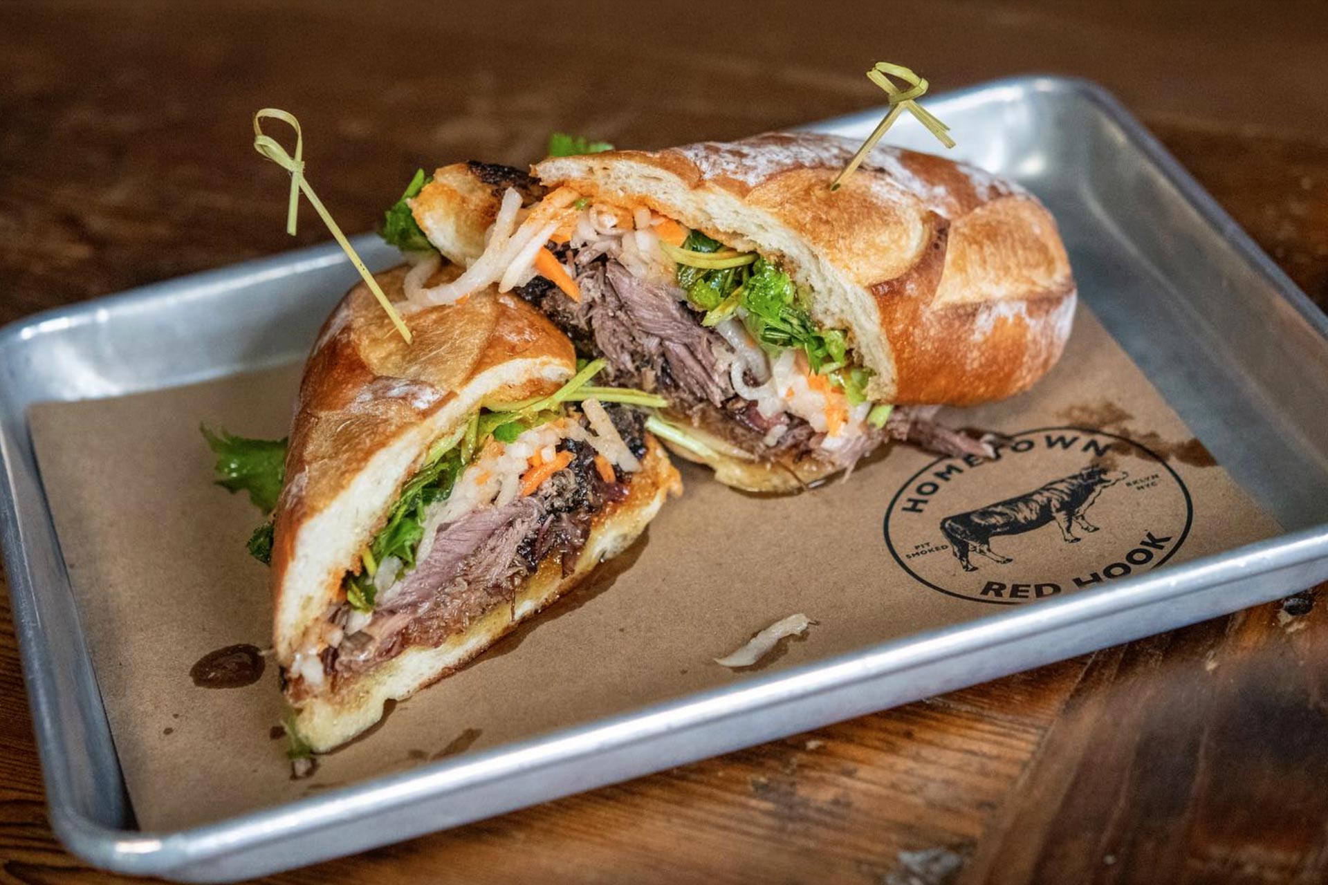 Smoked lamb belly piled on a crisp baguette with pickled carrot and daikon, hot and sweet sauce, and sprigs of fresh cilantro. © Hometown Bar B Que New York